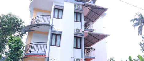A multi-story building with balconies, air conditioning units, and a covered entrance.