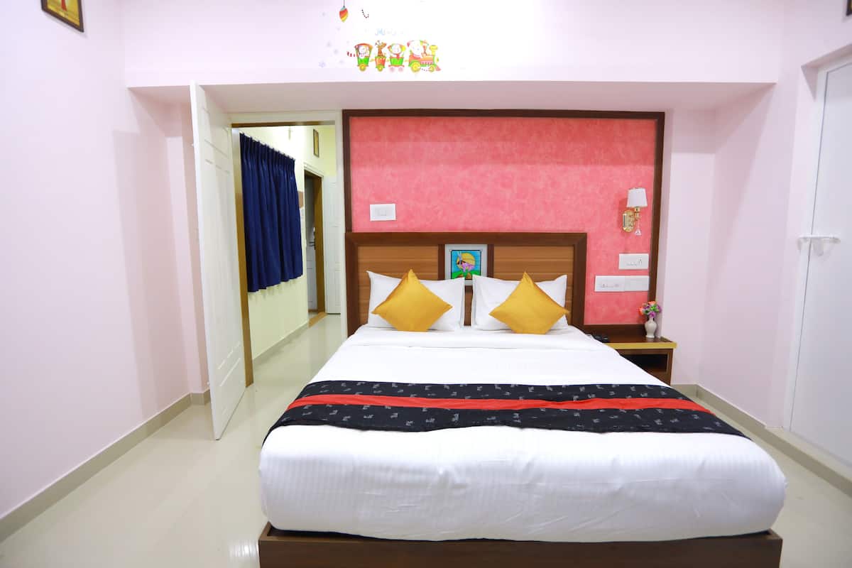A neatly made bed with white bedding and a black and red striped blanket, a wooden headboard, and a nightstand with a lamp and a small vase with flowers.