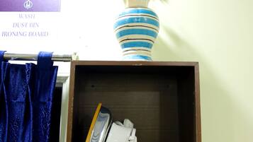 Una estantería con una tabla de planchar, un florero azul y blanco a rayas, y un letrero encima.