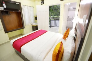 A hotel room with a bed, a TV mounted on the wall, a door leading to a balcony, and a bathroom visible through an open door. - Base9 Airport Hotel (Aluva)