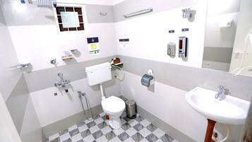 A bathroom with a toilet, sink, and shower. There are multiple handrails and a trash can.