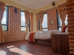 A room with a brick wall, a bed, a nightstand, and a window with curtains. - Hotel Layaku Durbar (Bhaktapur)