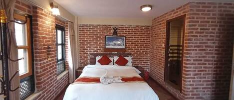 A room with a brick wall, a bed with white bedding, red pillows, and a framed picture on the wall.
