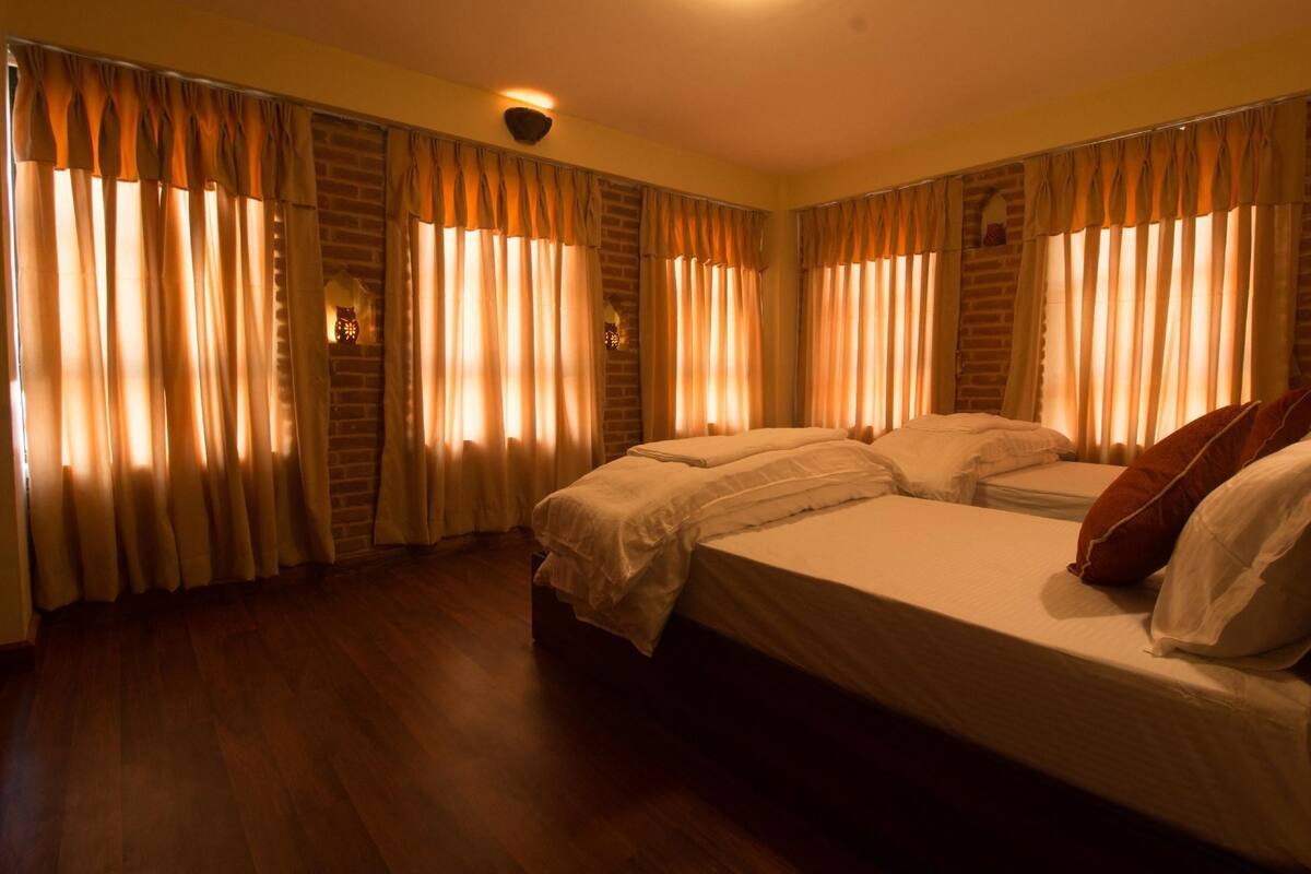 Quarto de hotel com duas camas, piso de madeira e cortinas nas janelas.