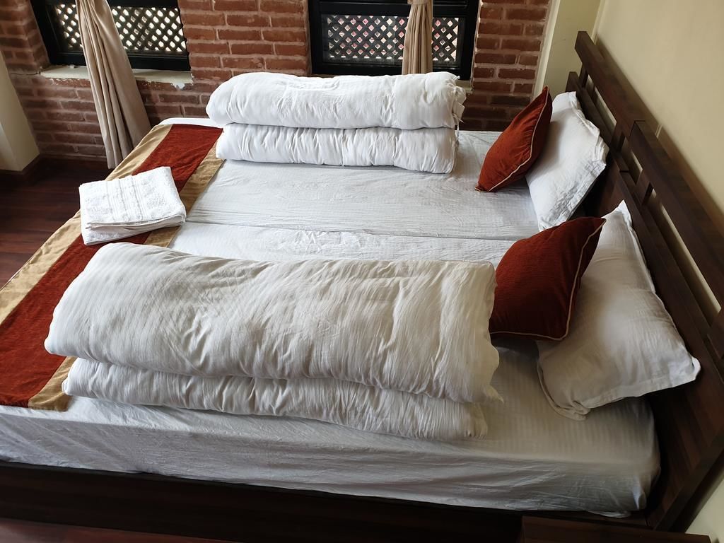 Ein ordentlich bezogenes Bett mit weißen Laken und braunen Kissen, ein hölzernes Kopfstück und im Hintergrund eine Backsteinwand mit einem Fenster.