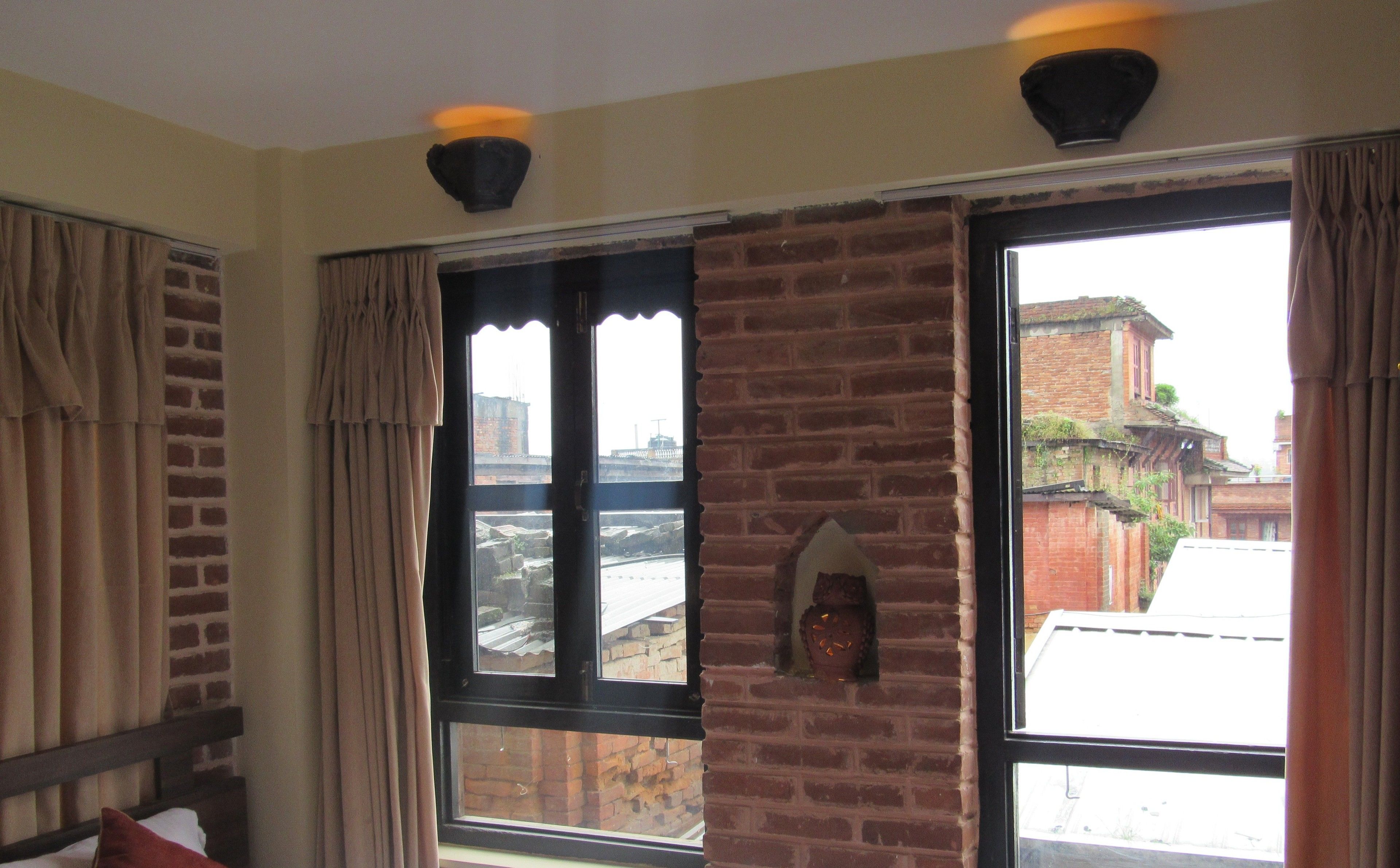 A room with a brick wall, a large window, and a bed with a pillow.