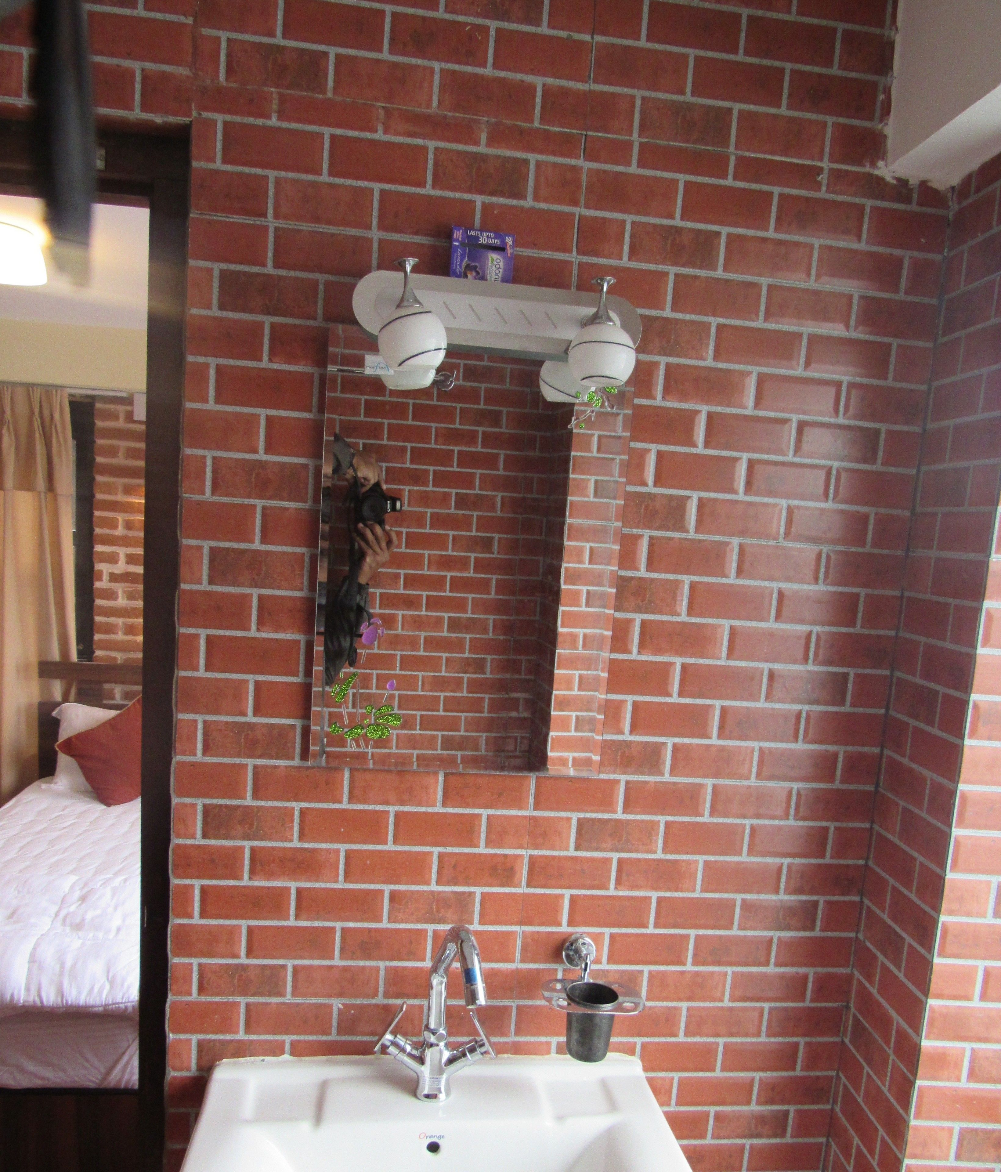 Une salle de bain avec un mur en briques rouges, un lavabo blanc, un miroir et une étagère contenant des articles de toilette.