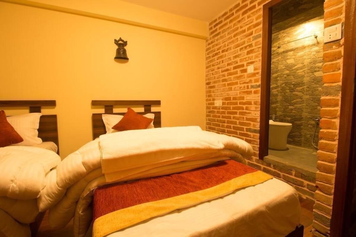 Quarto com duas camas, parede de pedra e janela com vista para um banheiro.