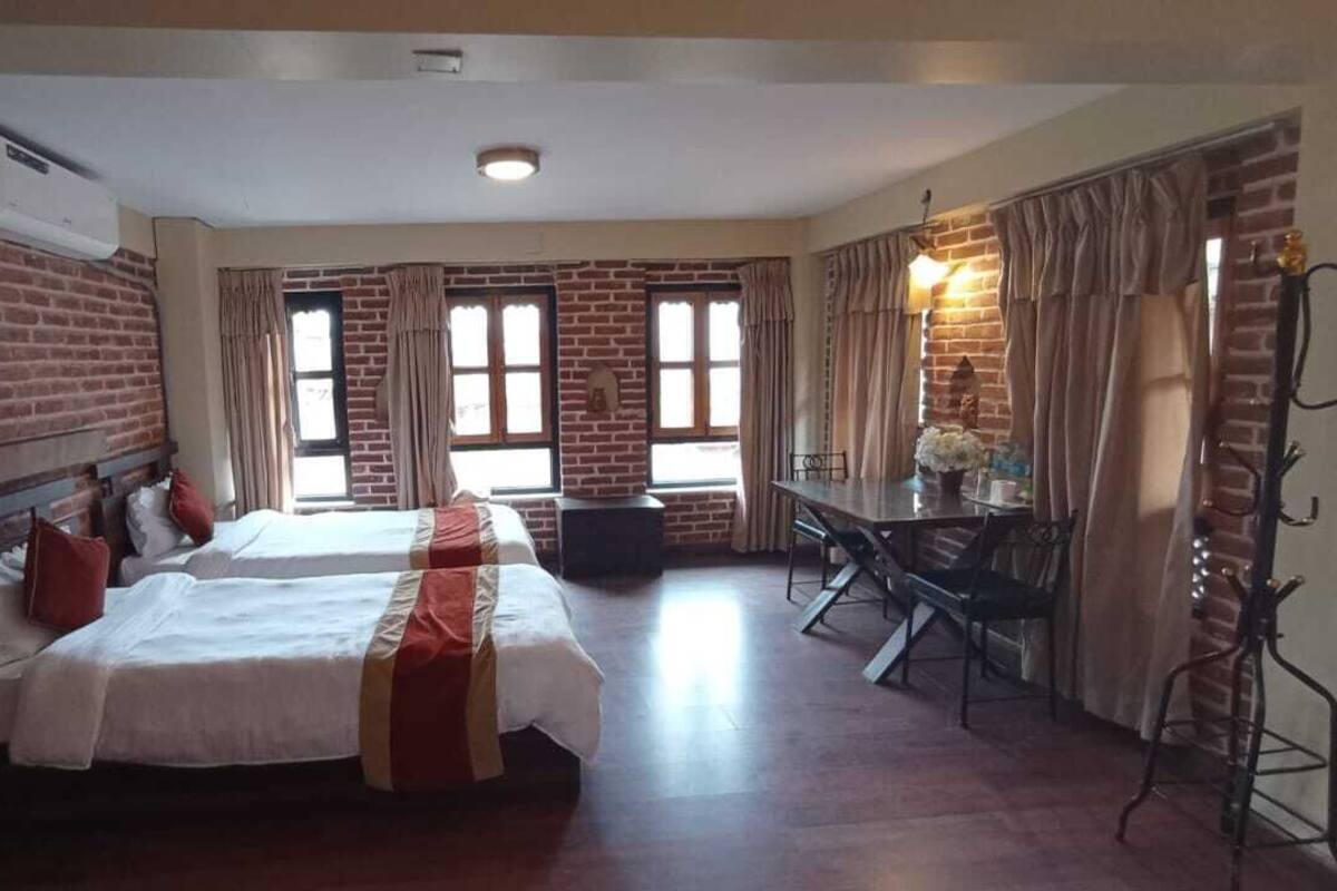 Quarto de hotel com duas camas, uma mesa de jantar e uma parede de tijolos.