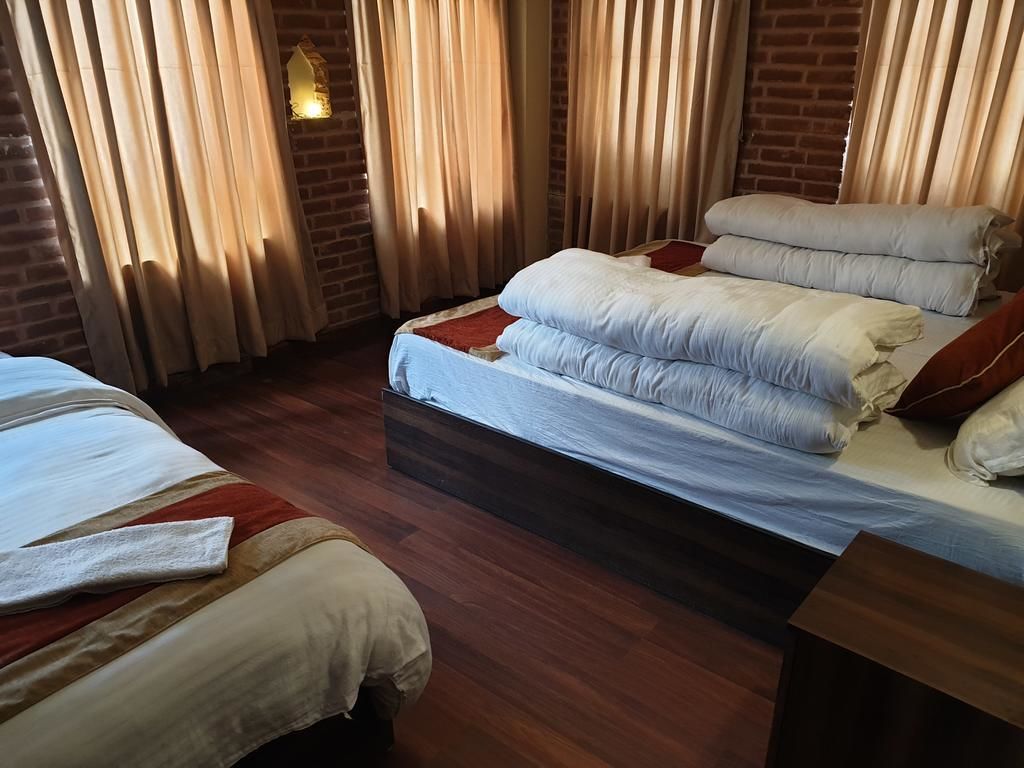 Habitación de hotel con suelo de madera, una cama con muchos almohadones, una mesita de noche y una lámpara fijada a la pared.