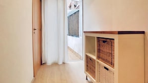 Un couloir avec un plancher en bois, une porte blanche et un rideau blanc. On y trouve un meuble en bois avec des paniers en osier.
