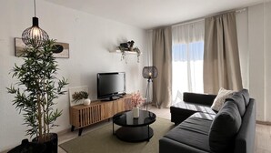 A modern living room with a black sofa, a wooden TV stand, a large potted plant, and a floor lamp.