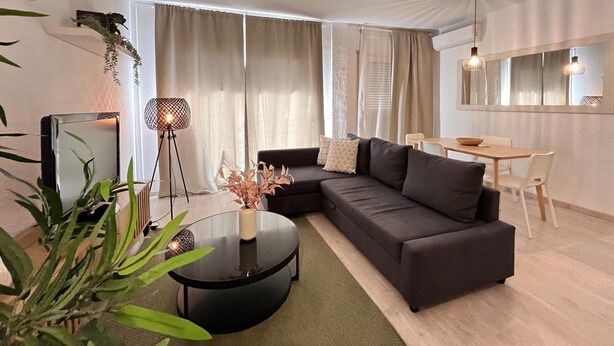 A modern living room with a sectional sofa, a round coffee table, a TV, and a dining area with a table and chairs.