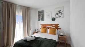 A bedroom with a bed, curtains, a wooden headboard, bedside tables, and wall art.