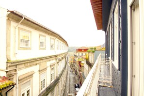 Uma rua estreita com edifícios de ambos os lados, um corrimão de metal à direita e um carro estacionado no meio.