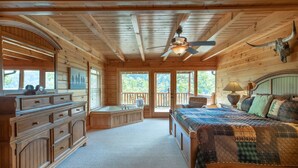 A wooden cabin bedroom with a large bed, a vanity with drawers, a bathtub, and a ceiling fan. - Luxurious cabin with Hot Tub & incredible views (Sevierville)