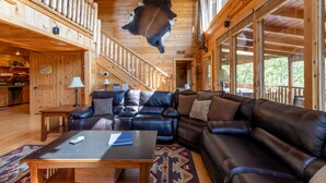 Ein Holzblockhaus-Interieur mit Ledersofa, montiertem Tierfell und einer Treppe, die zu einer oberen Ebene führt.