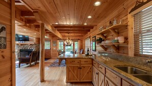 Ein Holzhütten-Interieur mit einer Küche, die eine Granitarbeitsplatte, Holzschränke und einen Kamin aus Stein umfasst.