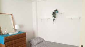 A small, neatly organized bedroom with a single bed, a wooden dresser, a mirror, and a wall-mounted shelf with a plant. - House near the sea and near the NEGOMBO spa complex (Lacco Ameno)