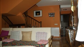 Una sala de estar con sofá, cojines estampados, una escalera y una zona de cocina.