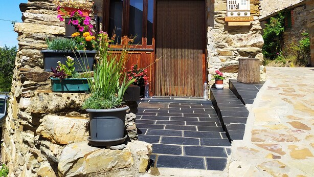 Una casa de piedra rústica con un balcón de madera, una puerta de madera y plantas en macetas en la entrada.