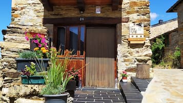 Uma casa de pedra rústica com varanda de madeira, porta de madeira e plantas em vasos na entrada.