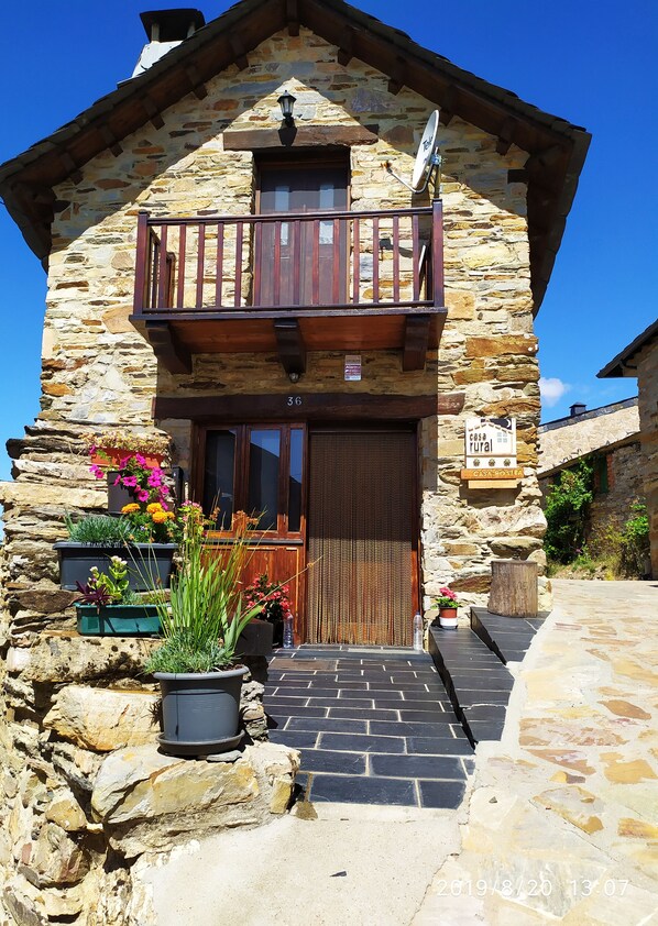 A rustic stone house with a wooden balcony, a wooden door, and potted plants at the entrance. - Cottage in Sierra de la Culebra, Biosphere Reserve. Wolf observation. (Santa Cruz de los Cuérragos)
