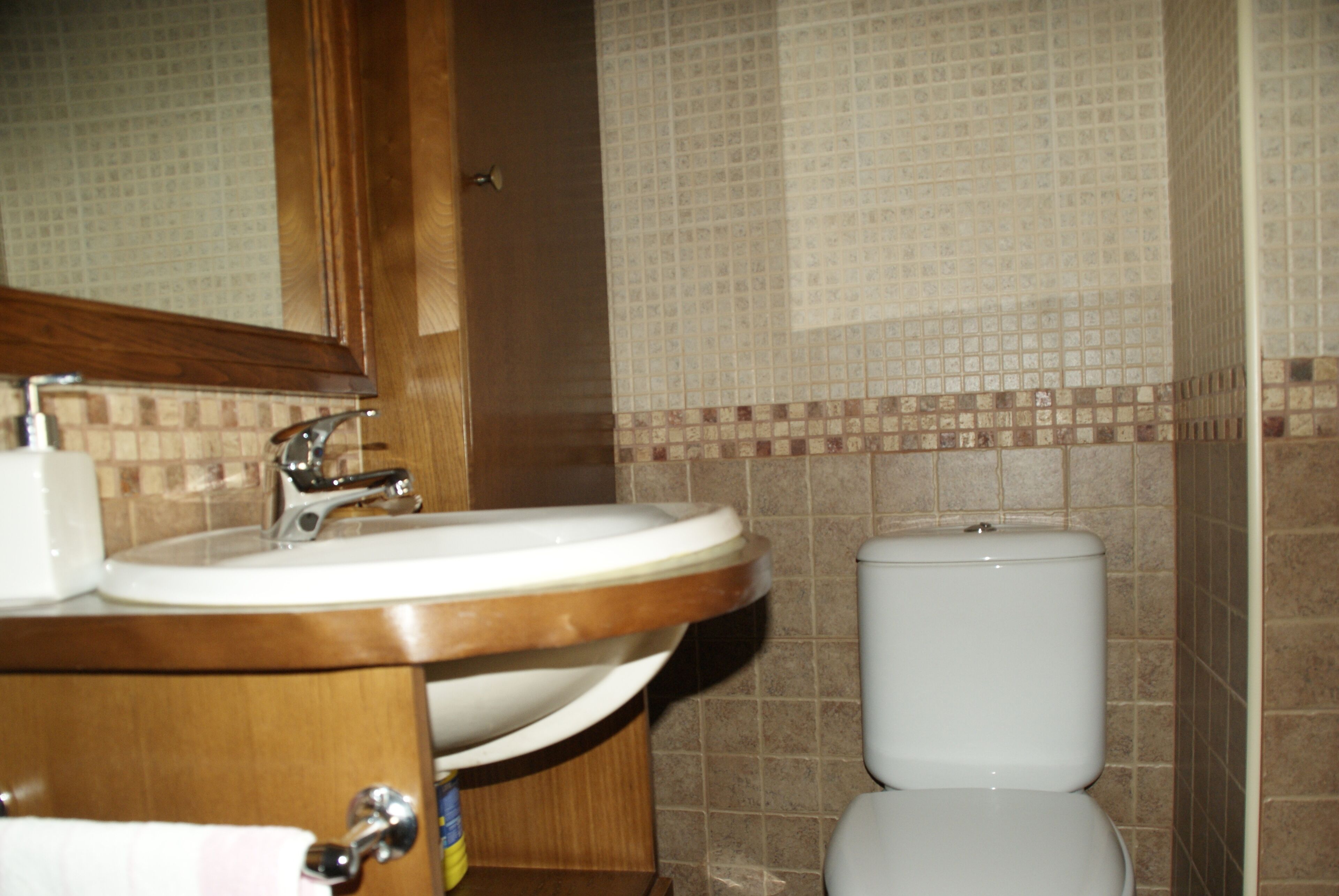 Un baño con tocador de madera, lavamanos e inodoro.