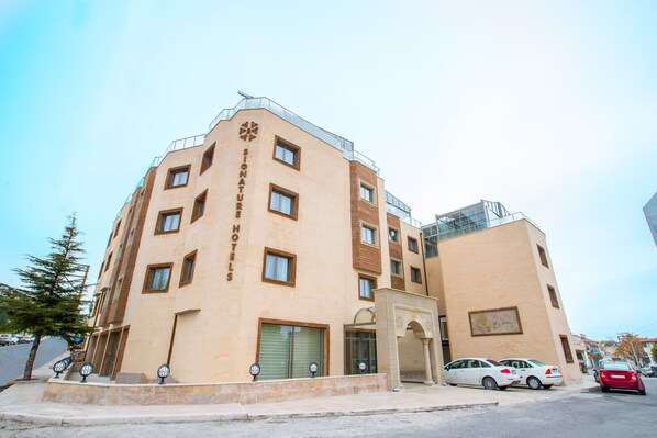 A multi-story hotel with a beige facade, a prominent logo, and a gated entrance. - Signature Hotels & Spa (Ürgüp)