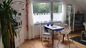 A dining area with a table and chairs, a radiator, a window with a view of greenery, and a plant. - Charming apartment between Bremen and Bremerhaven (Hagen im Bremischen)