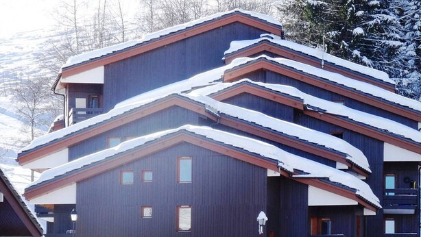 Un immeuble à plusieurs étages, doté d’une façade sombre et d’un toit recouvert de neige.