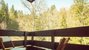 Une terrasse en bois avec deux chaises et une table, entourée d’une zone boisée.