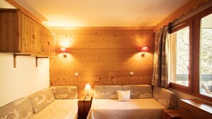 Une chambre confortable dans un chalet, avec des murs en bois, deux lits dotés de têtes de lit assorties, une petite table et deux lampes fixées au mur.