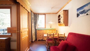 Une pièce chaleureuse aux murs en bois et dotée d’un canapé rouge. On y trouve une table à manger en bois avec des chaises, une fenêtre avec des rideaux et un tableau accroché au mur.