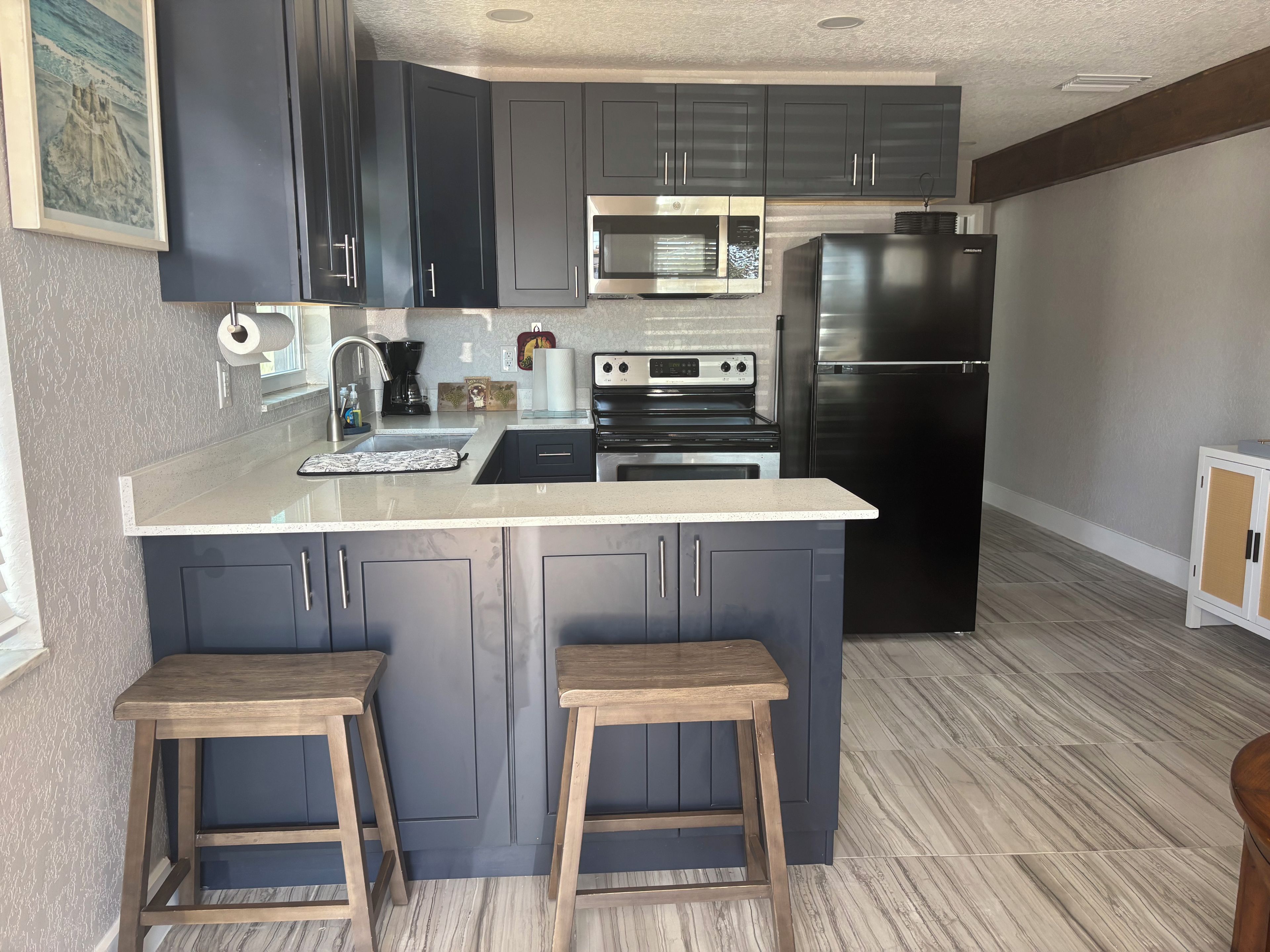 A modern kitchen with dark cabinets, stainless steel appliances, and a marble countertop.