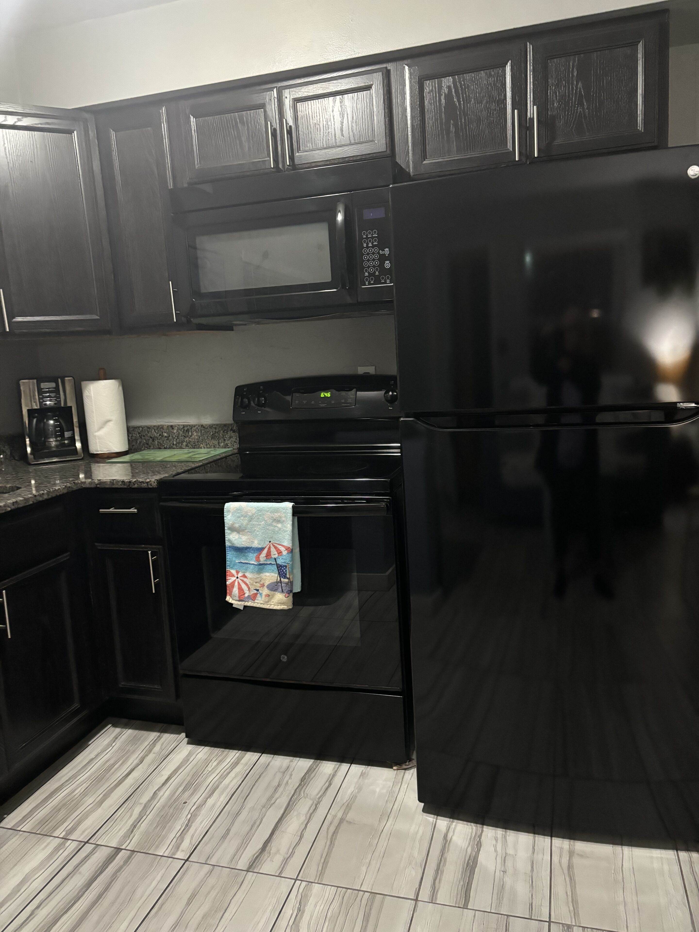 A kitchen with dark wooden cabinets, a black microwave, a stove, and a refrigerator.