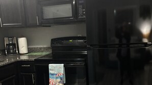 A kitchen with dark wooden cabinets, a black microwave, a stove, and a refrigerator. - VACATION RETREAT Madeira Beach (Madeira Beach)