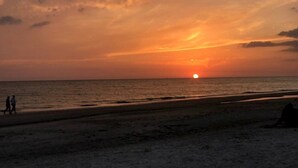A beach at sunset with a visible sun, calm sea, and two people walking. - VACATION RETREAT Madeira Beach (Madeira Beach)