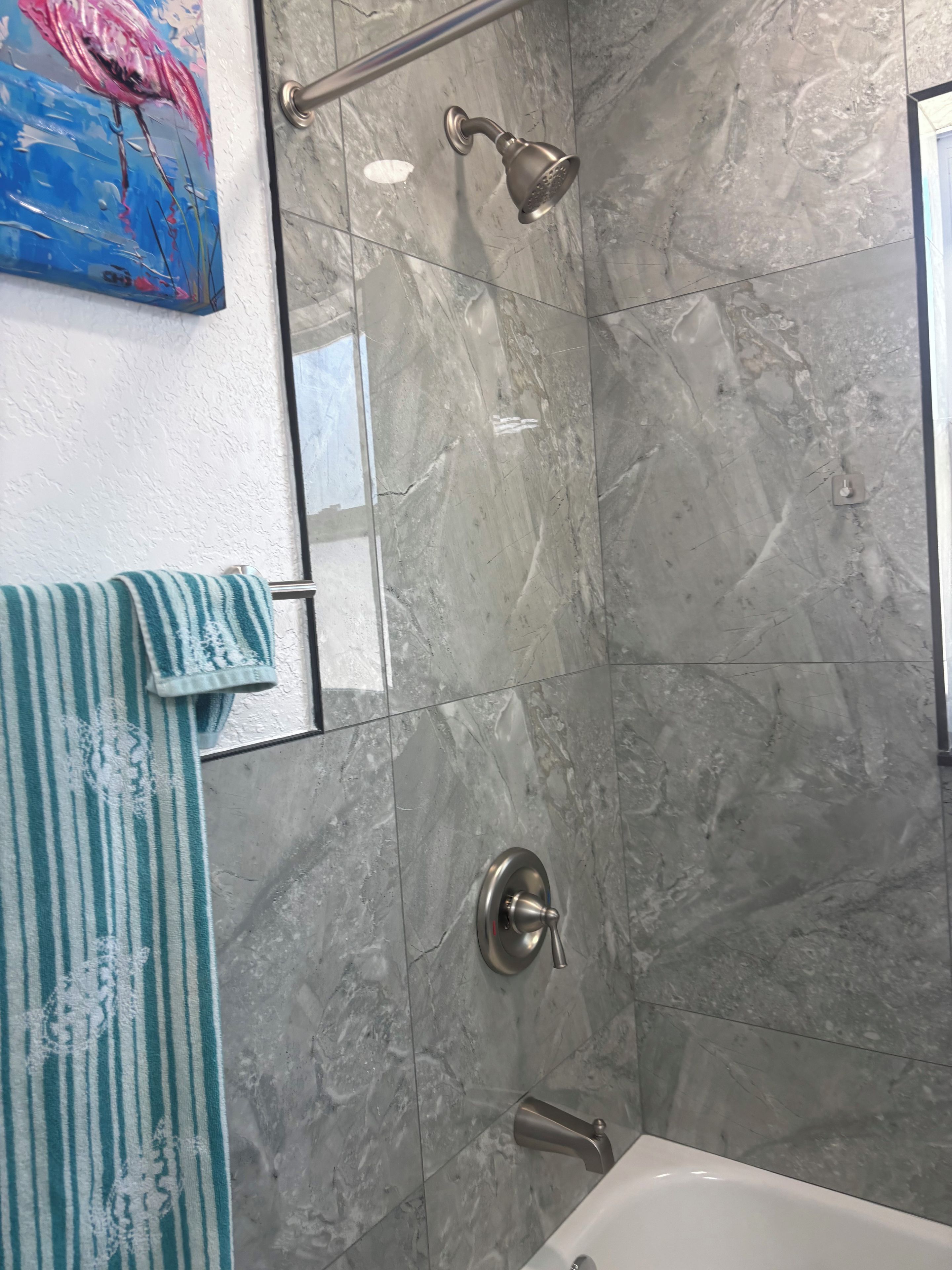 Un baño con ducha, toallero y una toalla a rayas, además de una pared de mármol.