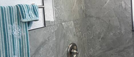 Un baño con ducha, toallero y una toalla a rayas, además de una pared de mármol.