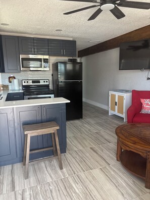 A modern kitchen with grey cabinets, a black refrigerator, a microwave, and a stove. There is a wooden stool and a round wooden table.