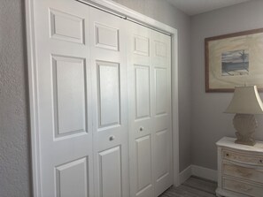A white door with a textured surface, a framed picture on the wall, and a white nightstand with a lamp.