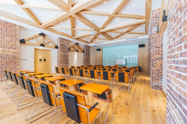 Un aula con pupitres y sillas de madera, paredes de ladrillo y techo de madera.