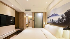 Una habitación de hotel con una cama grande, un televisor de pantalla plana, un escritorio y un cuadro de un paisaje montañoso en la pared.