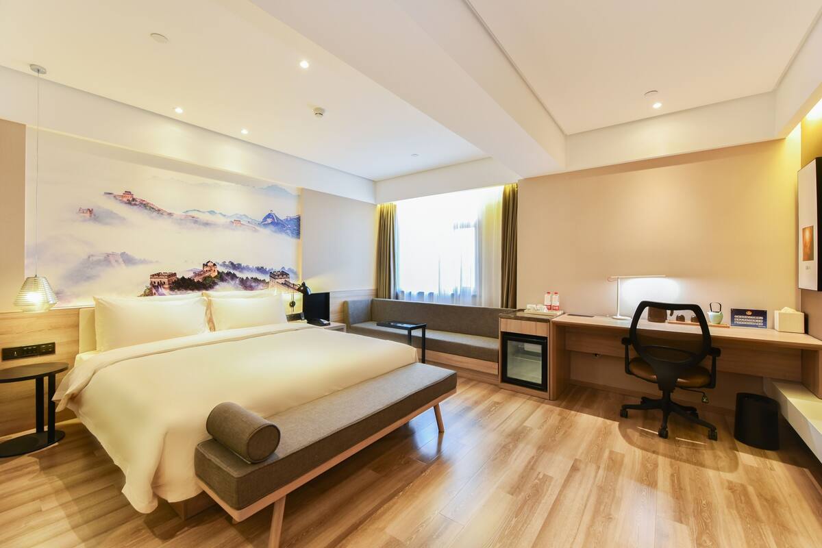Een moderne hotelkamer met een groot bed, een bureau, een stoel, een klein tafeltje en een tv aan de muur.