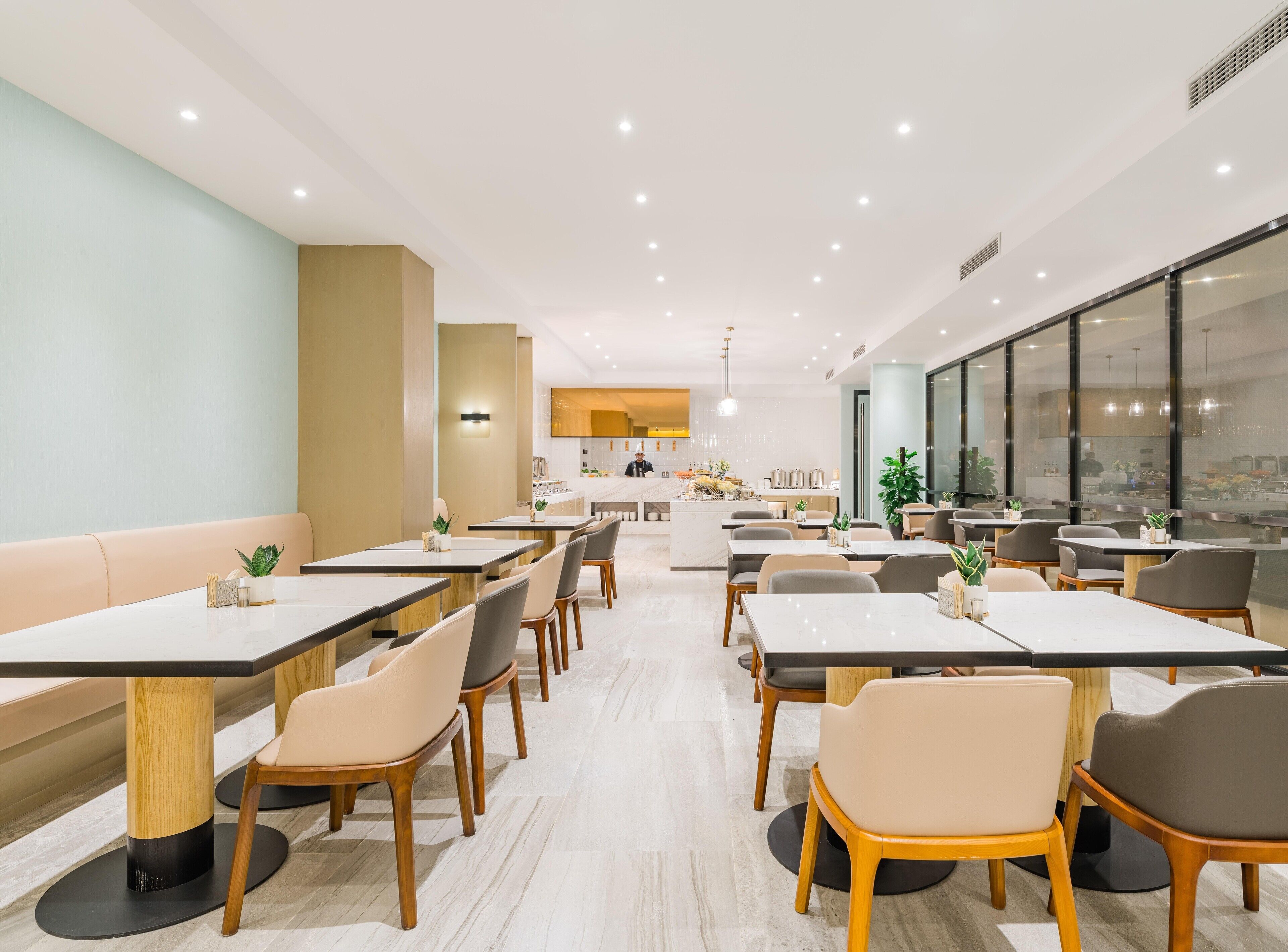 A modern dining area with multiple tables and chairs, a central island with a bar, and large windows providing natural light.