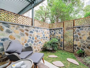 A stone wall with a bamboo fence, a small garden with stepping stones, and wicker furniture. - Atour Hotel Baimaiquan Shaungshan Ave Jinan (Jinan)