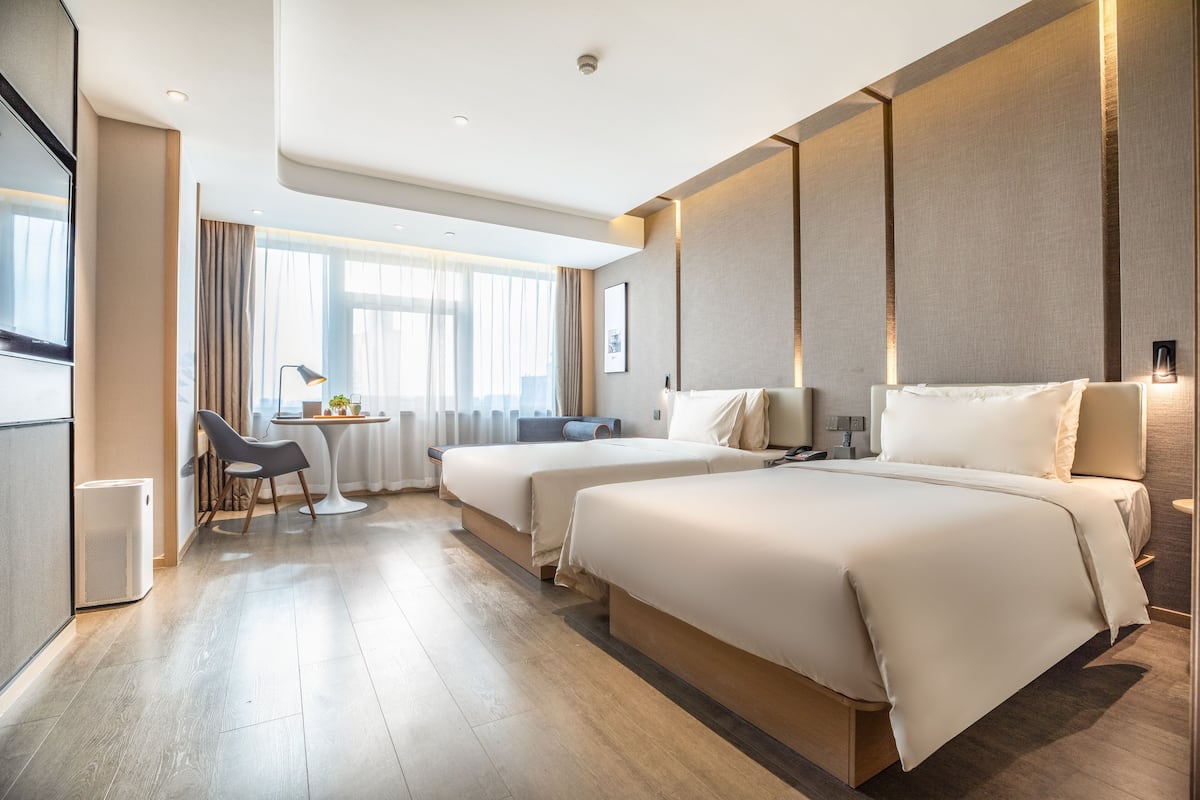 A hotel room with two beds, a desk, and a chair.