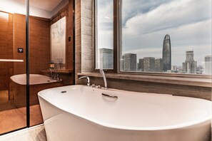Un baño moderno con una bañera grande, un lavamanos independiente y un ventanal con vistas a la ciudad.