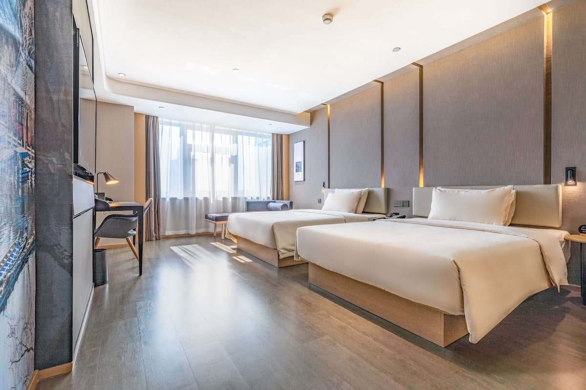 A modern hotel room with two beds, a desk, and a large window.